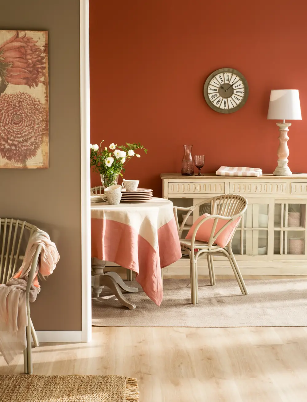 Comedor con pared color teja y marrón, aparador en crema con puertas de cristal, reloj, lámpara de sobremesa y mesa redonda de comedor con silla