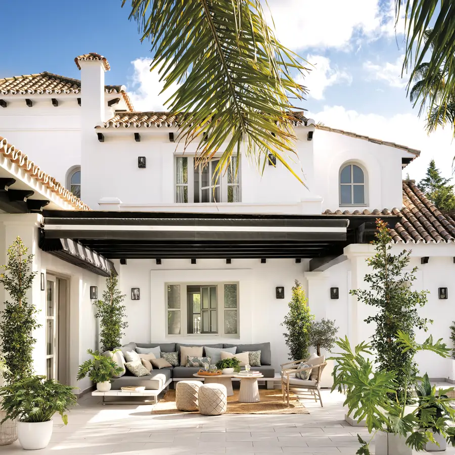 fachada con porche, salón exterior con sofá esquinero, puf, alfombra, plantas, suelo de piedra
