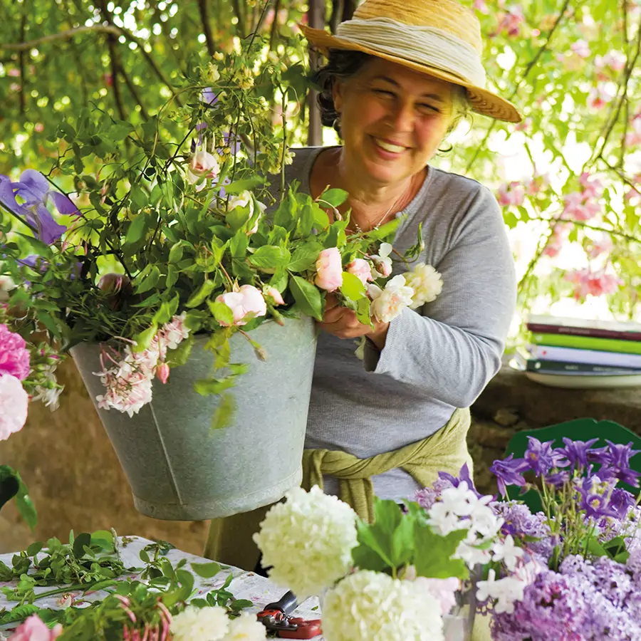 Mujer con sobrero de paja sujetando cubo de rosas con utensilios de jardinería