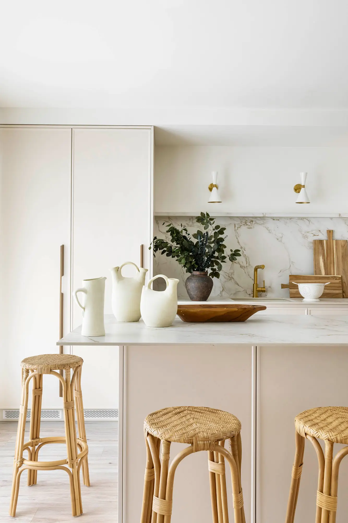 Cocina blanca con isla y taburetes de bambú.