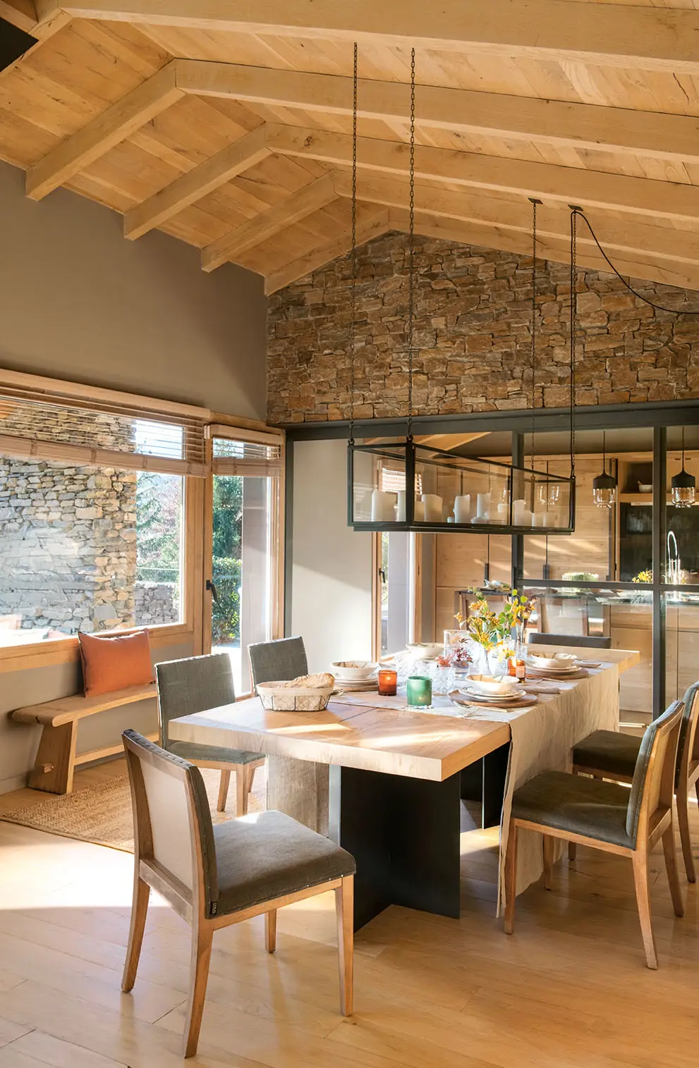 Una mesa de comedor de madera y acero, con sillas de madera y lámpara de techo de acero con velas