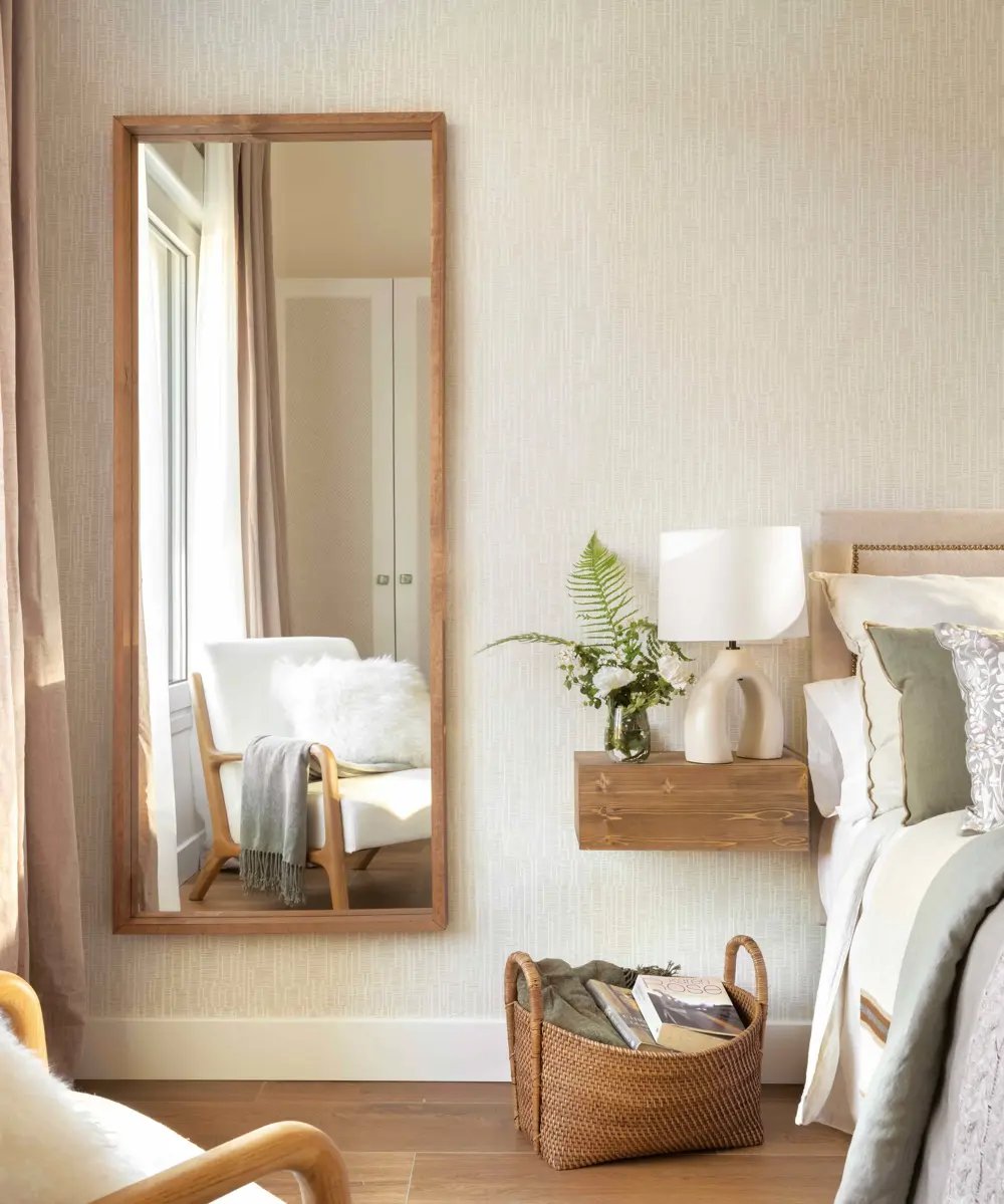 00584103 dormitorio espejo butaca mesita noche madera volada cesta libros mantas tonos beige verde crema cojin de pelo