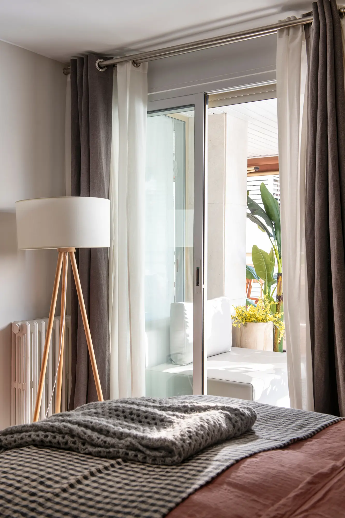 Dormitorio con ventana vestida con doble cortina, lámpara de pie y radiador.