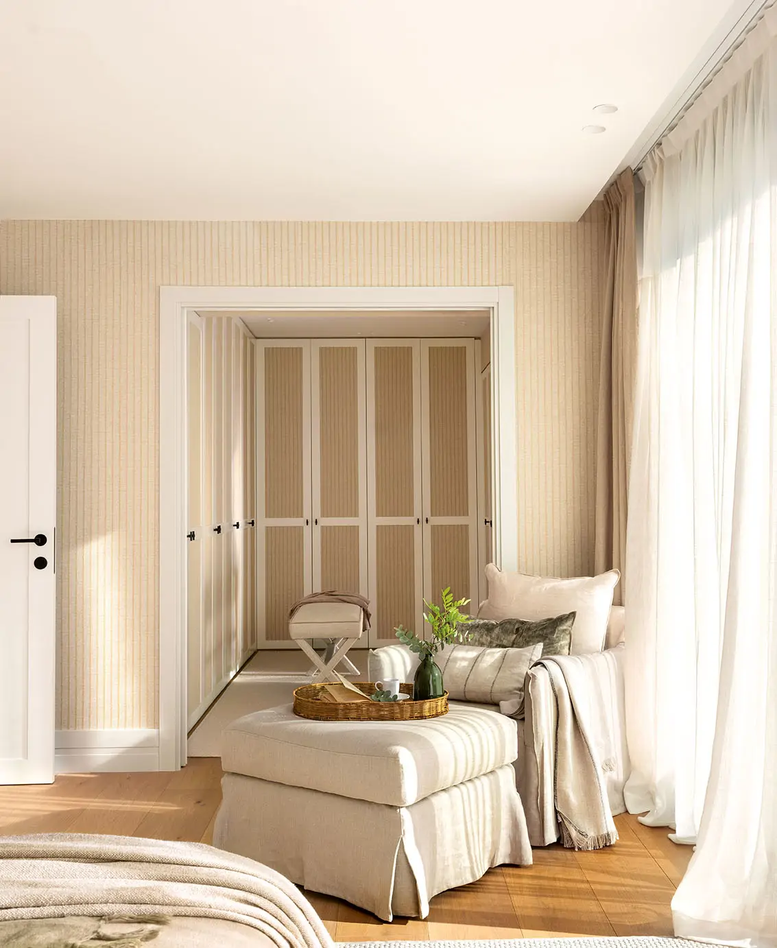 Una zona de lectura en el dormitorio con sofá y reposapiés en lino beige