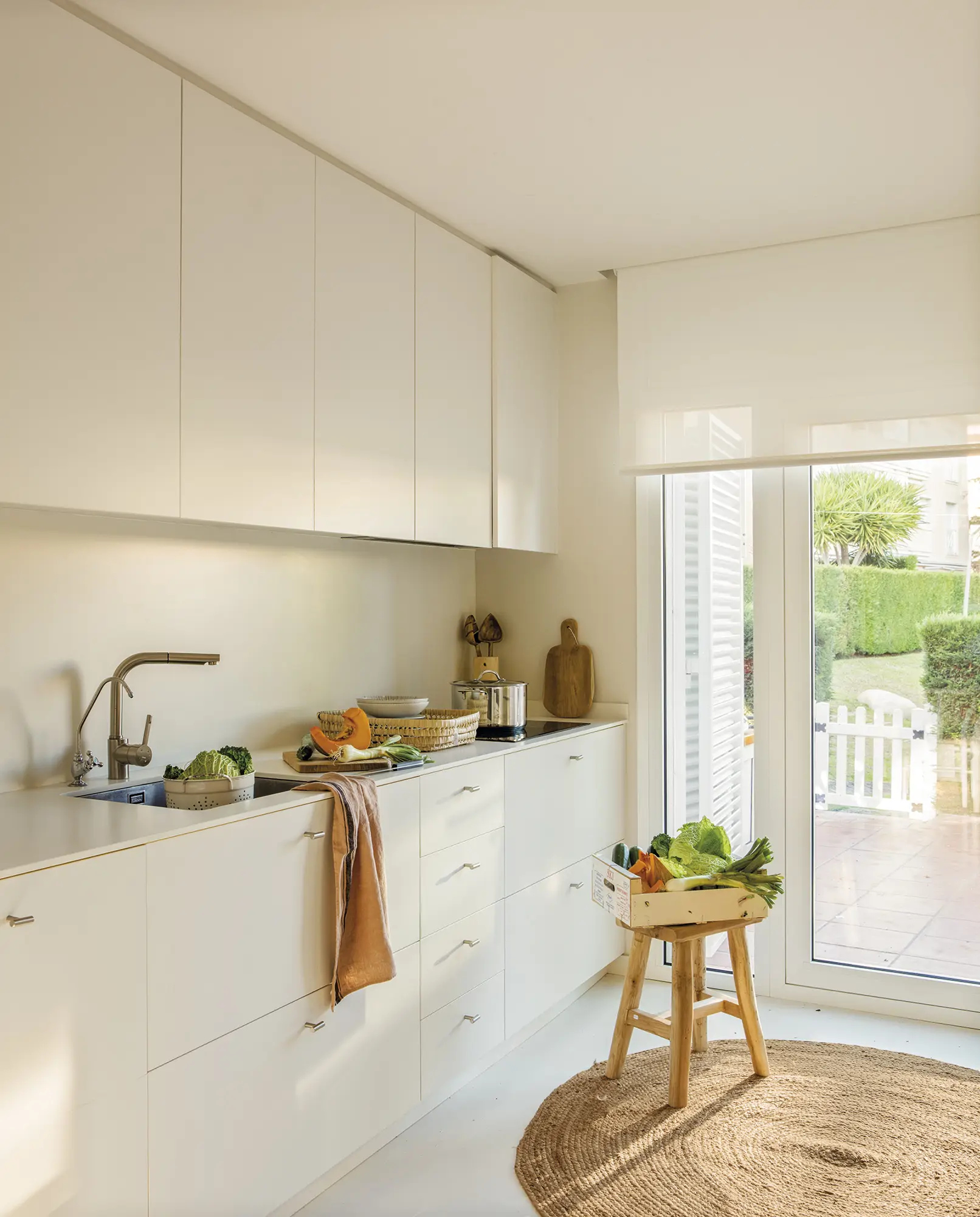 Cocina blanca con suelo de microcemento, taburete de madera y alfombra de fibras