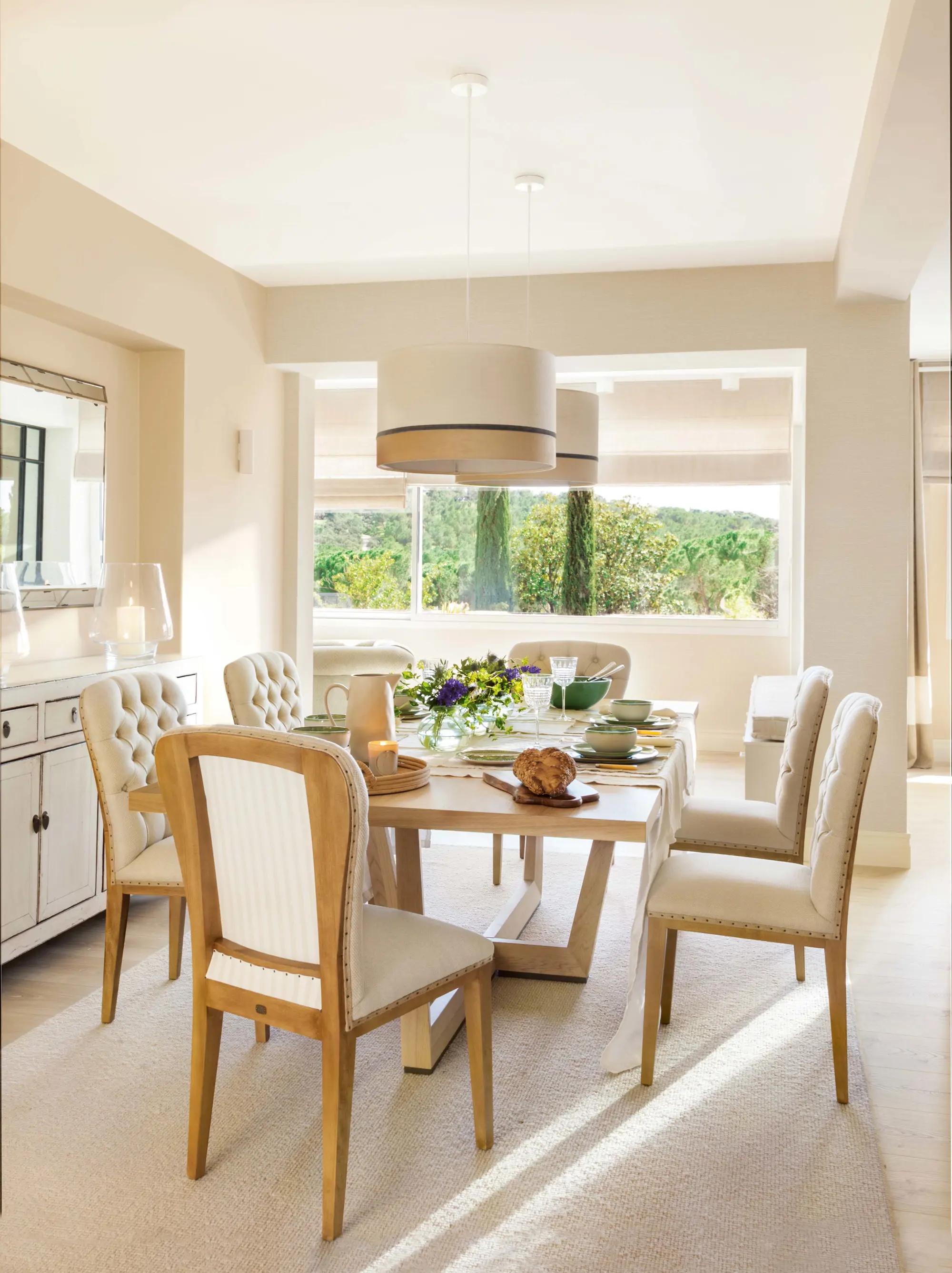 Comedor con mesa de madera rectangular, sillas tapizadas con asiento capitoné y lámparas suspendidas