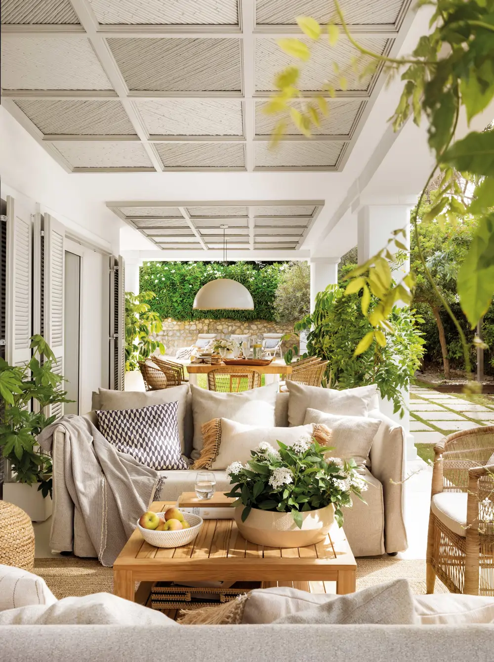 Porche cubierto con salón y comedor rodeado de plantas