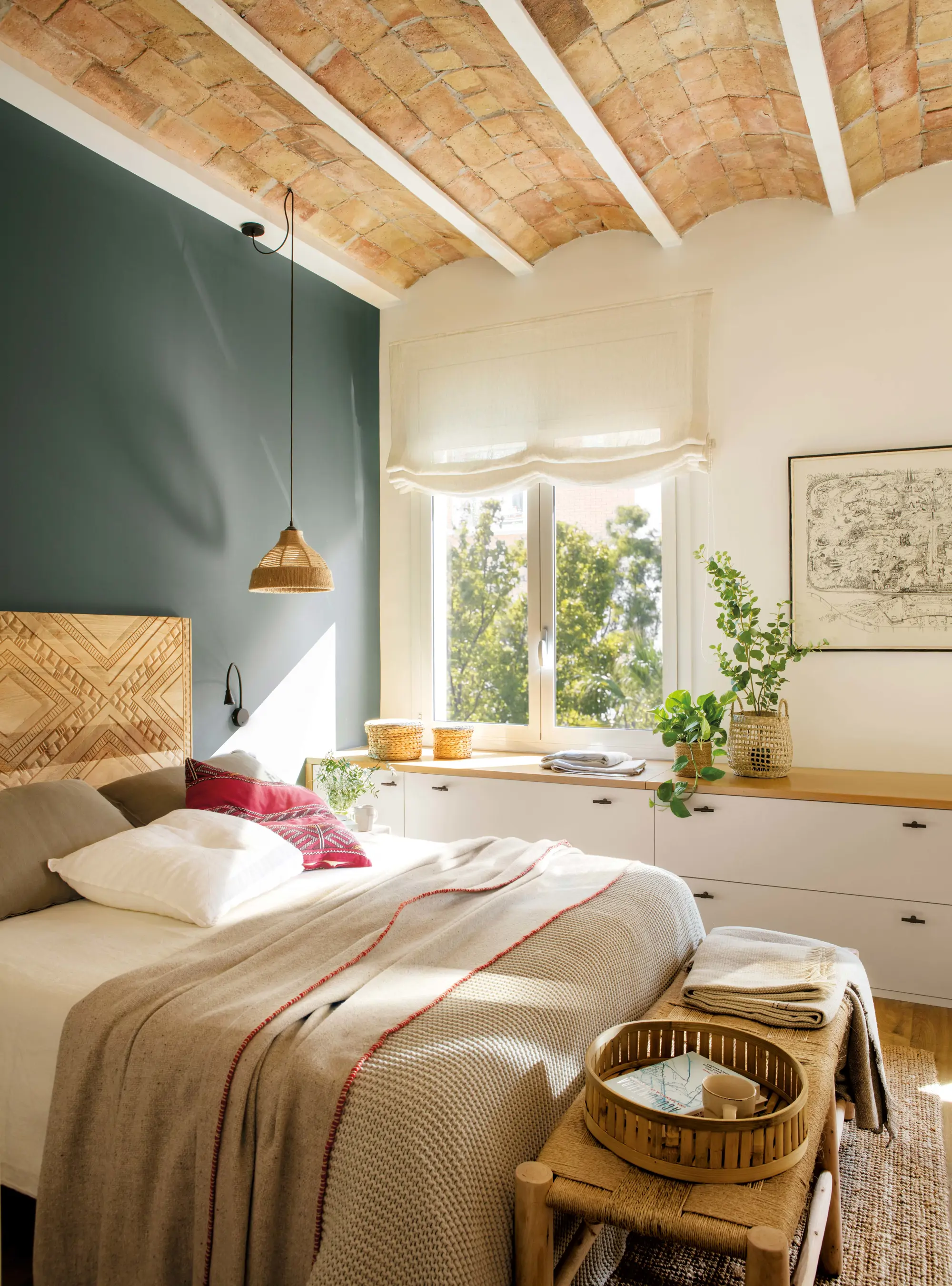 Dormitorio con cabecero de madera, pared pintada de verde y mueble bajo la ventana